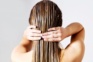Blond woman applying hair conditioner. Isolated on white.