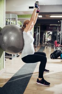 Pregnant woman doing exercises with hand handles and fitness ball in gym