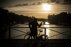 A woman stands with a bicycle as the sun rises along the banks of the Seine river, on October 18, 2016 in Paris. / AFP / LIONEL BONAVENTURE (Photo credit should read LIONEL BONAVENTURE/AFP/Getty Images)